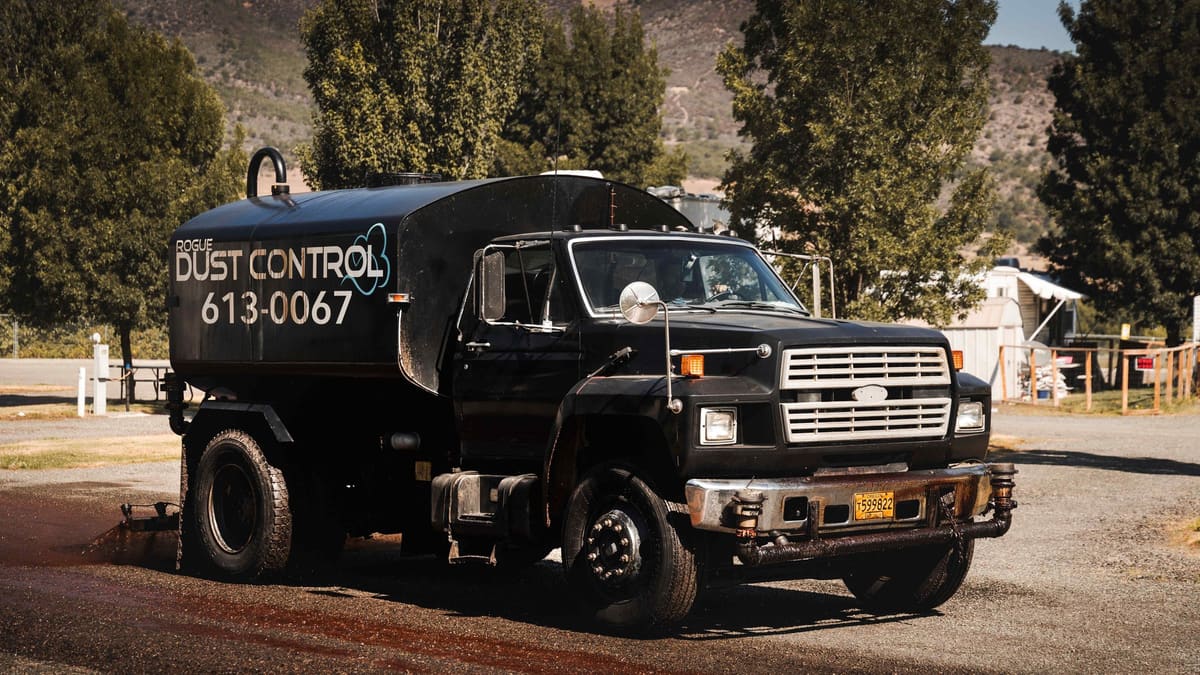 The black tanker spraying a gravel road beside an RV park.