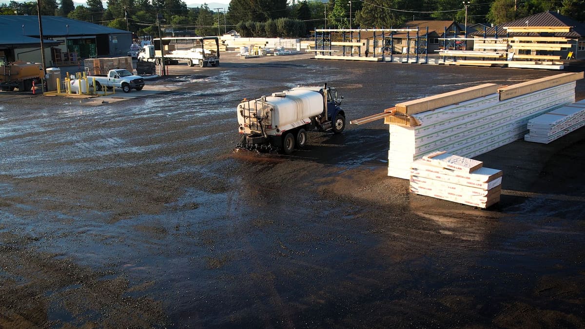 Drone view of the white tanker working across a lumber yard lot beside stacked boards.
