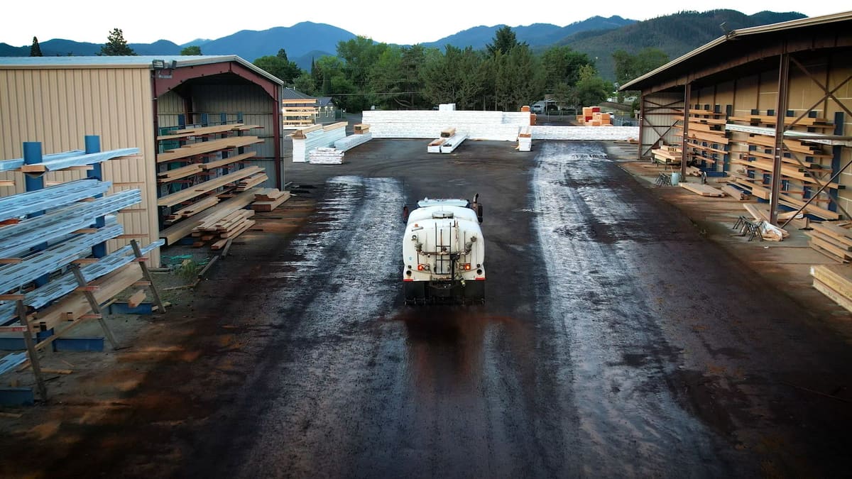 Drone view of a white tanker treating the drive aisle of a lumber yard.