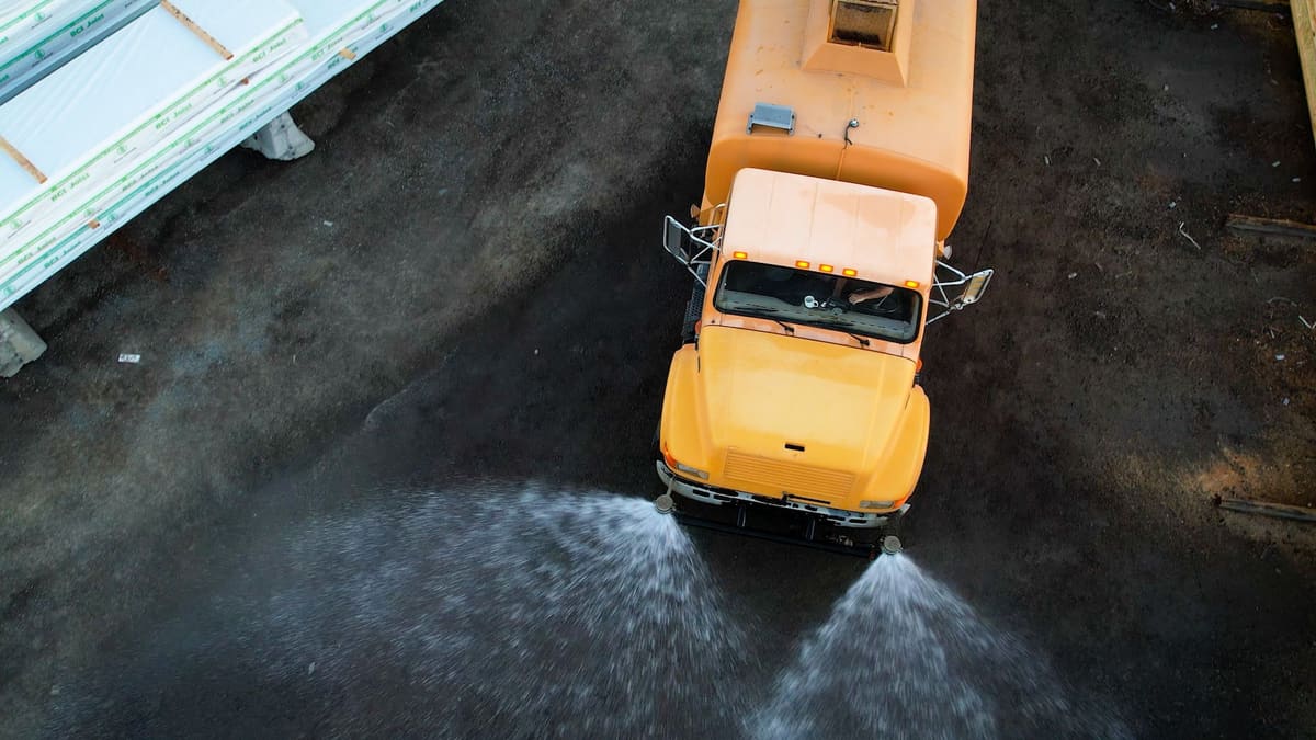 Drone view straight down on the yellow tanker spraying a dirt lot.