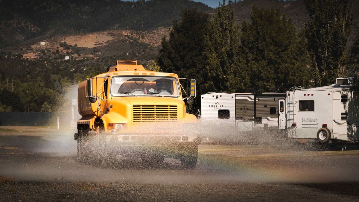 The yellow tanker spraying a gravel road past parked RVs.